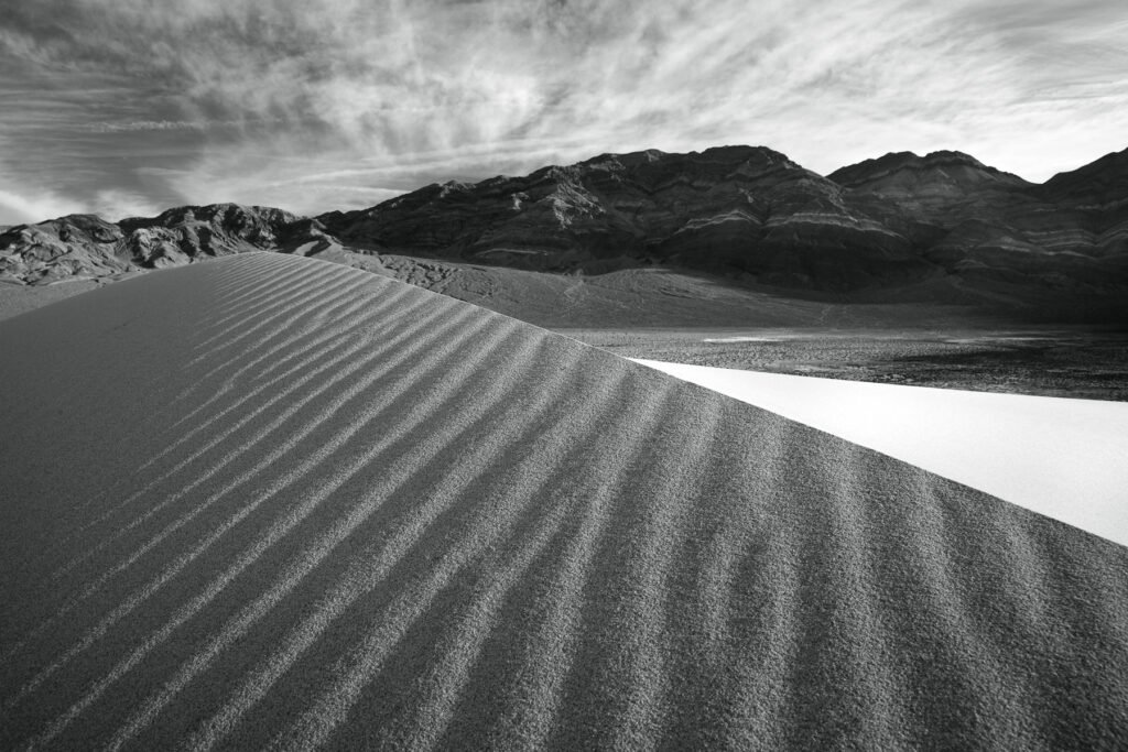 Black rocks with trails in Death Valley's Racetrack Playa desert floor against mountain backdrop.