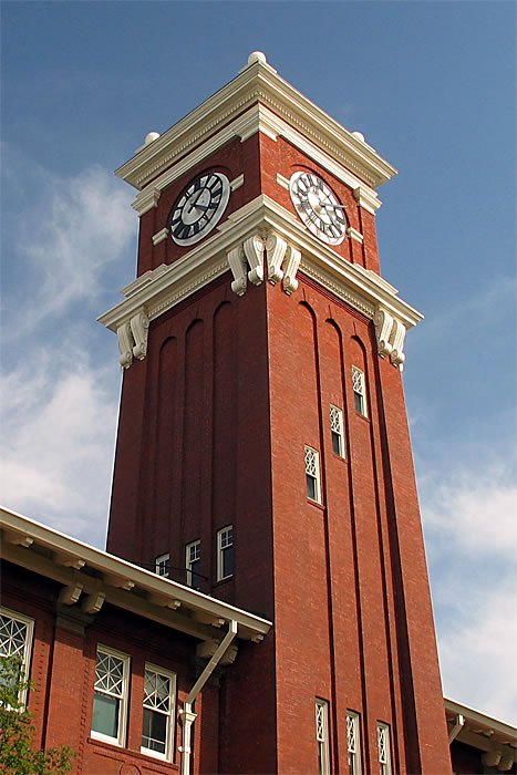 A tall red brick clock tower with white trim is shown against a clear blue sky. Multiple angles of the historic structure are displayed in a collage format.