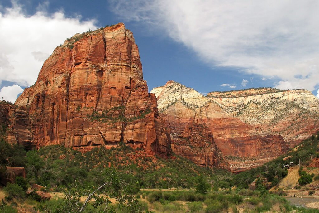 Majestic red rock cliffs rise against a bright blue sky with scattered clouds.