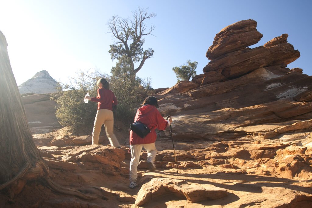 Two hikers navigating rugged red rock formations under a clear sky.