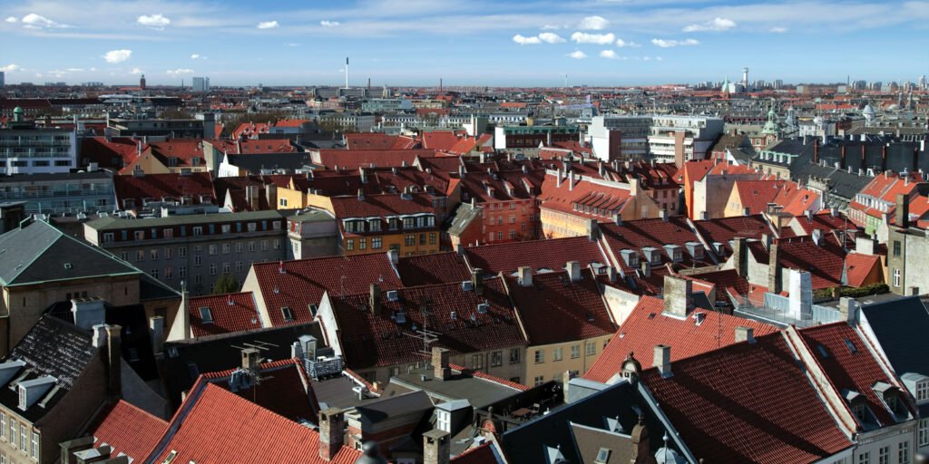 Panoramic shot of densely packed buildings with vibrant red roofs under a partly cloudy sky.