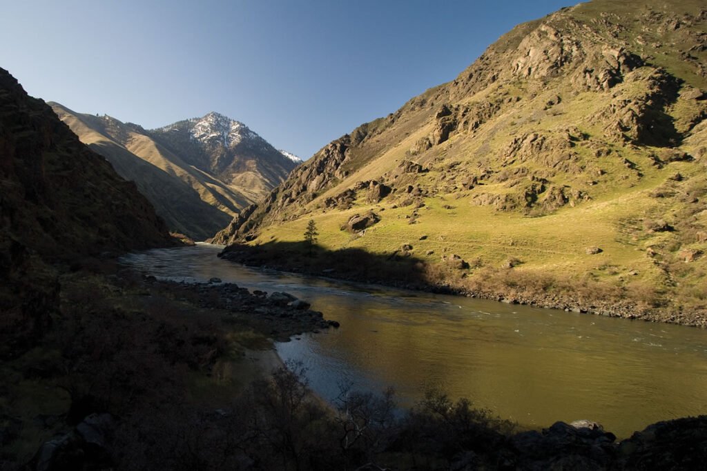 A scenic view of a river flowing through a mountainous valley with snow-capped peaks in the background.