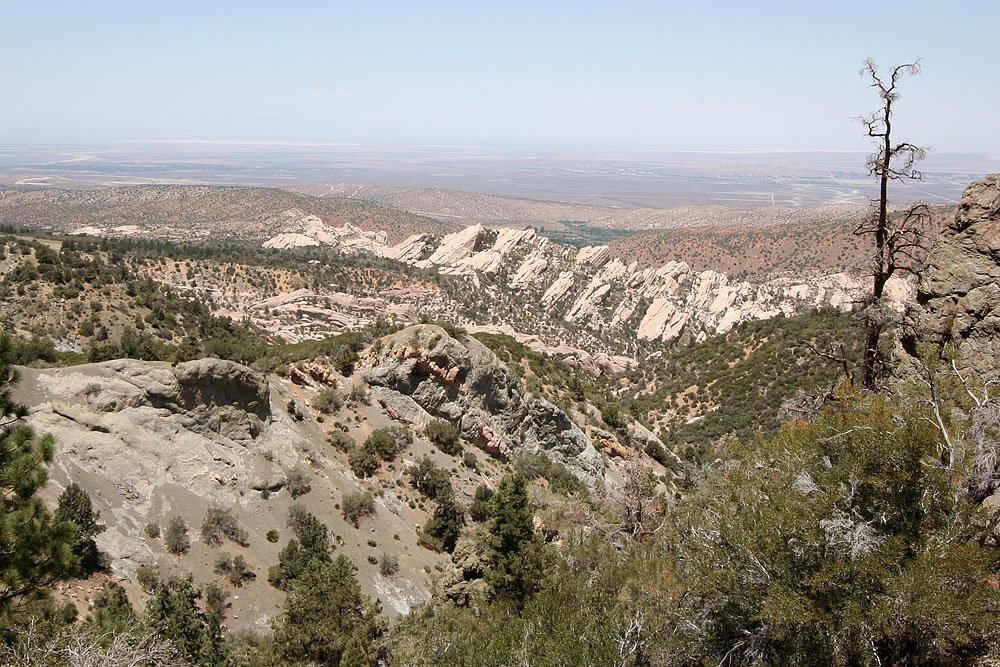 The image is split into three parts. The top part shows a rocky hillside with sparse green vegetation and a clear blue sky in the background.
