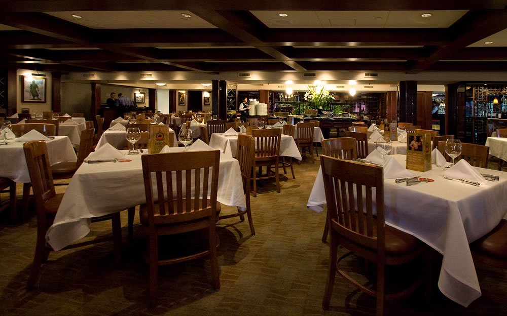 The elegant dining room aboard a luxury train, featuring white tablecloths, wooden chairs, and warm lighting.