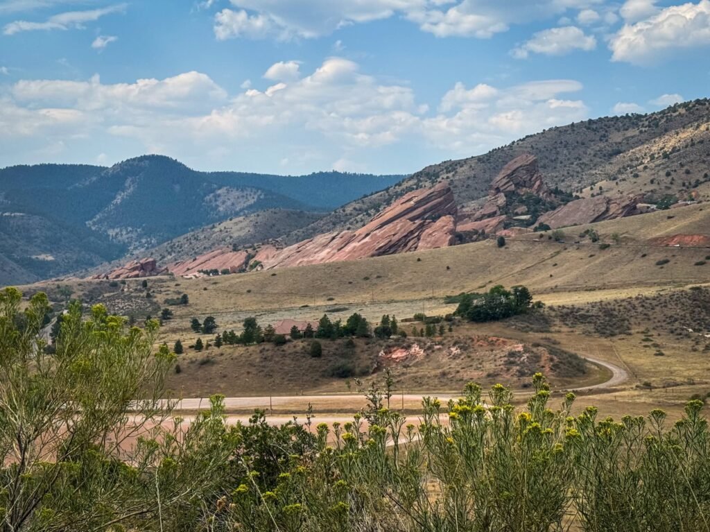 A panoramic view showcasing rolling hills, lush greenery, and a bright blue sky with scattered clouds.