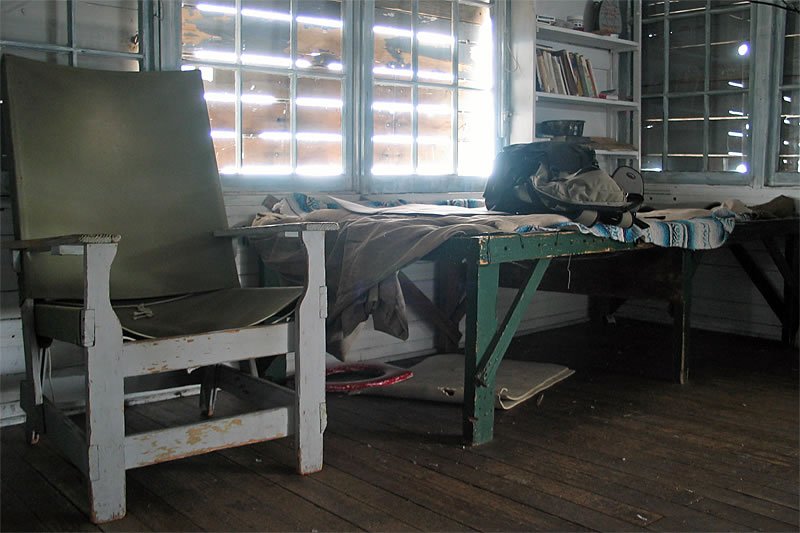 A vintage writing desk and peeling paint chair sit in a rustic home office, bathed in natural light from large windows.