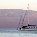 The Whaler on Kaanapali A serene sailboat floats near red hills under a pastel sky.