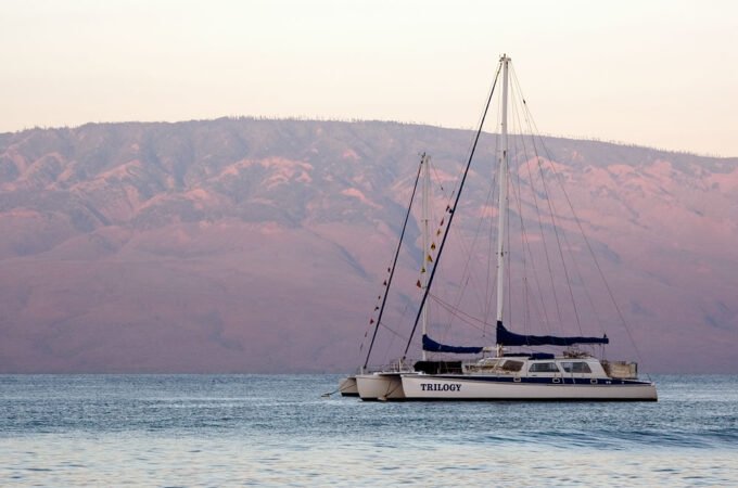 A serene sailboat floats near red hills under a pastel sky.