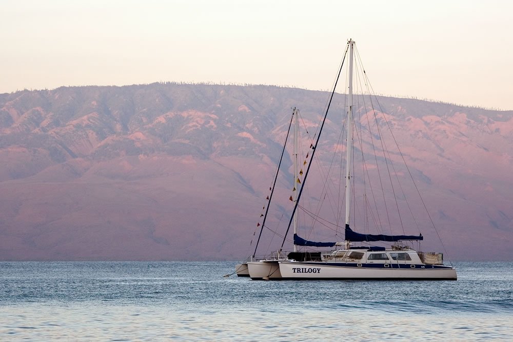 A serene sailboat floats near red hills under a pastel sky.