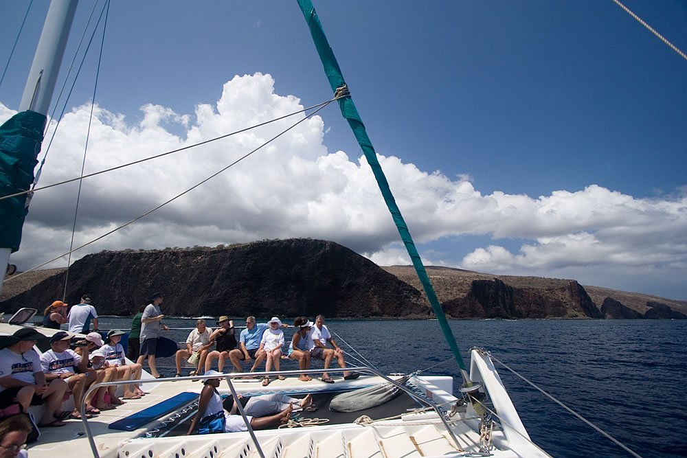 Two photos: one shows a sailboat with passengers enjoying a sunny day near dramatic cliffs, and the other highlights the sailboat's mast against a backdrop of blue skies and fluffy clouds.