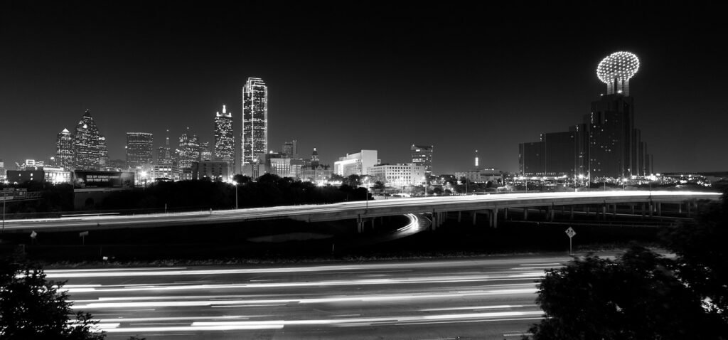 A stunning black and white photo of the San Antonio skyline at night with light trails on a bridge.
