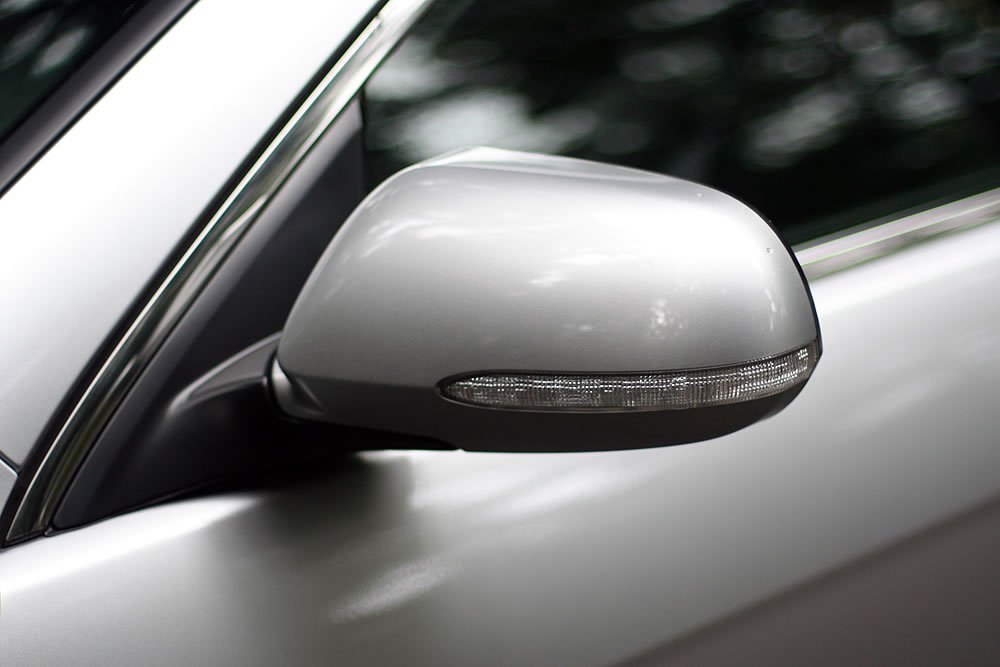 A close-up view of a silver car side mirror with integrated turn signal, showcasing clean lines and modern design.