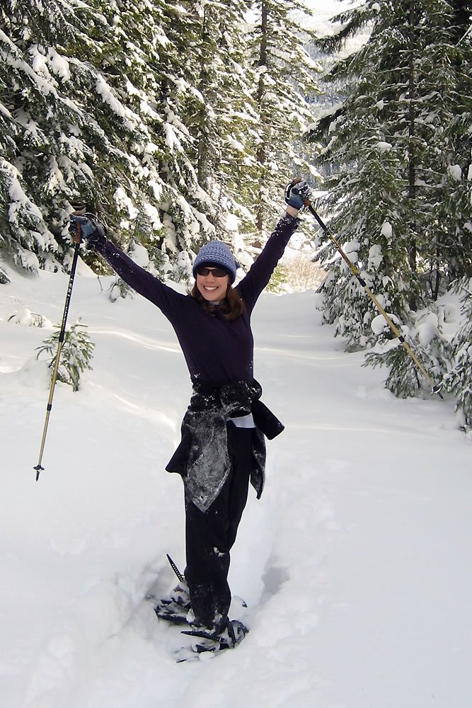 A joyful skier stands triumphantly in a snow-covered forest, arms raised high.