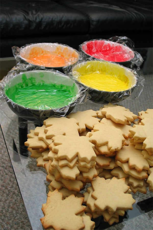 Snowflake-shaped sugar cookies next to bowls of colorful icing. Homemade treats prepared for holiday season.