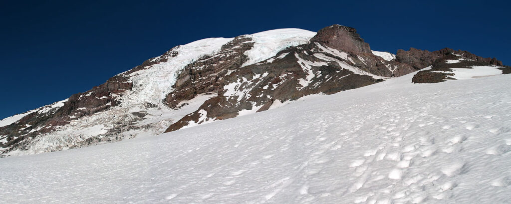 A snow-covered mountain peak with rocky outcrops under a clear blue sky.
