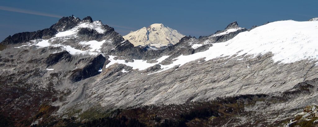 Majestic snow-capped mountains rise under a clear blue sky, showcasing the rugged beauty of the Pacific Northwest landscape.