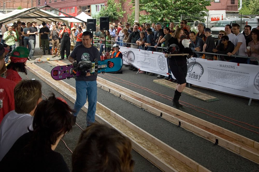 Two soapbox cars racing down wooden tracks while spectators watch.