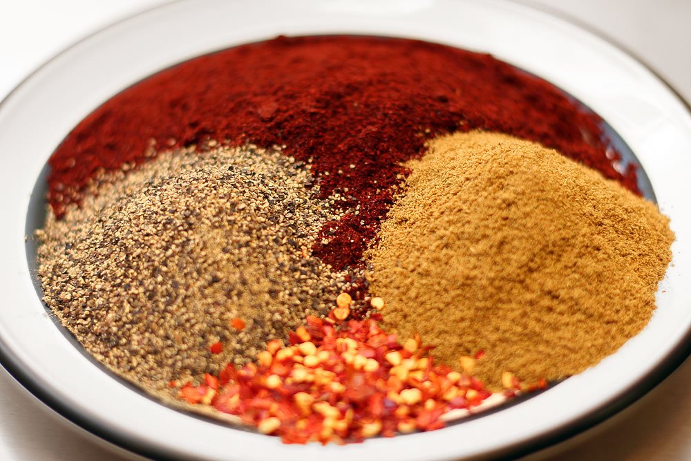 A plate divided into sections with vibrant red paprika, earthy cumin, and fiery red pepper flakes.