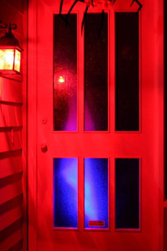 A front door illuminated with red and blue lights for Halloween, featuring spider decorations. This festive setup welcomes visitors with a spooky ambiance.