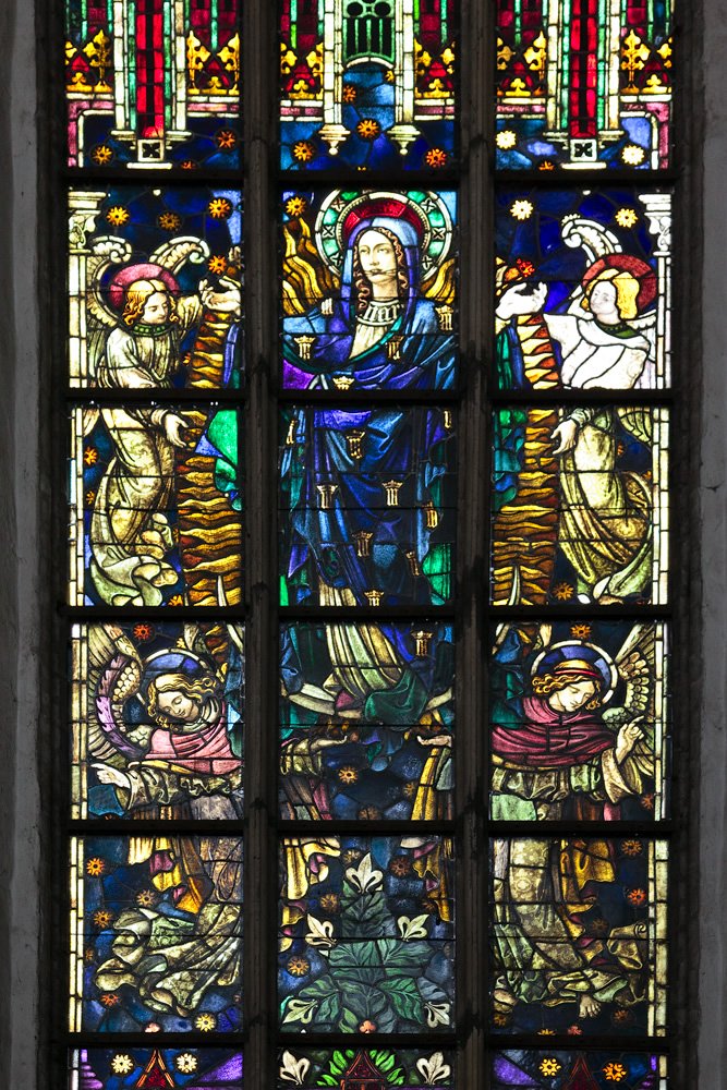 A vibrant stained glass window featuring angelic figures and intricate color patterns, framed by stone columns.