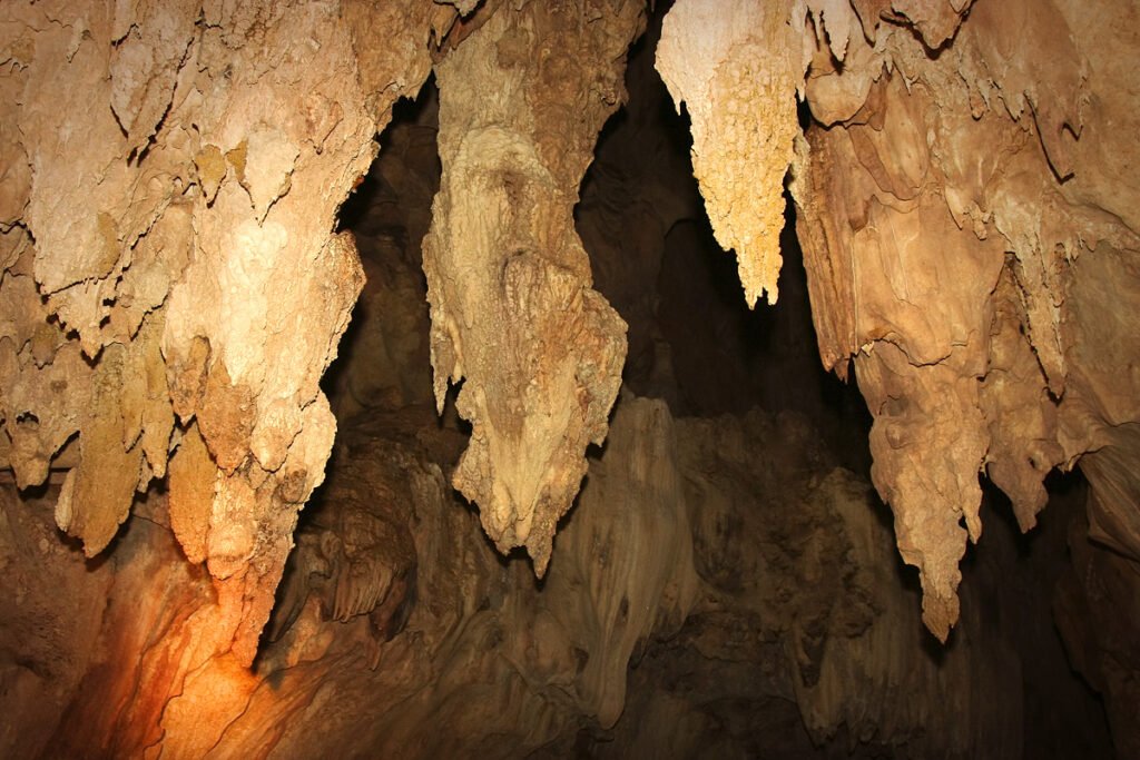 A collection of stalactites hanging from the cave ceiling, illuminated by a warm light source within the cavern.