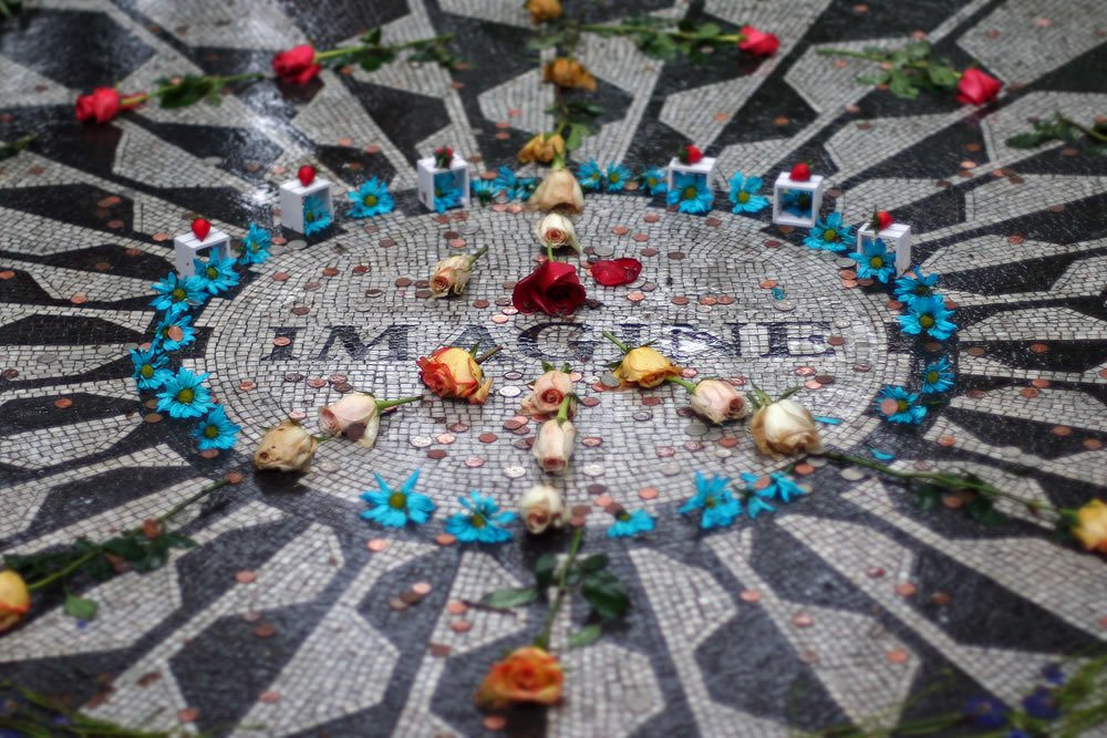 A close-up of the 'Imagine' mosaic in Central Park adorned with flowers and candles as a tribute.