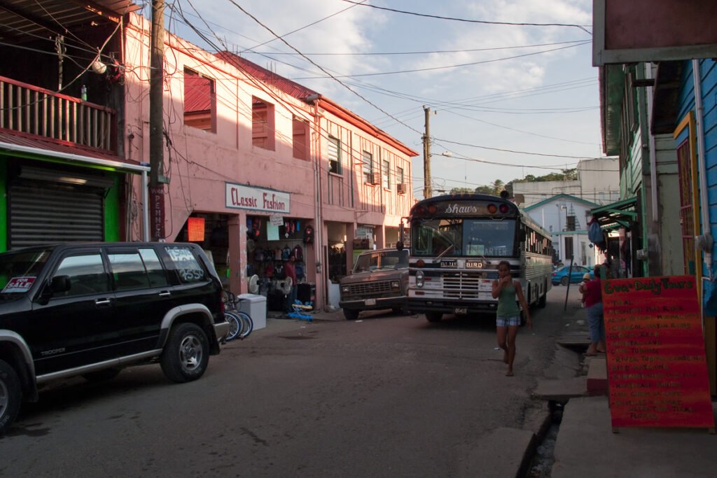 A street view showing parked vehicles, including a black SUV and a truck, alongside colorful building facades with shops and balconies.