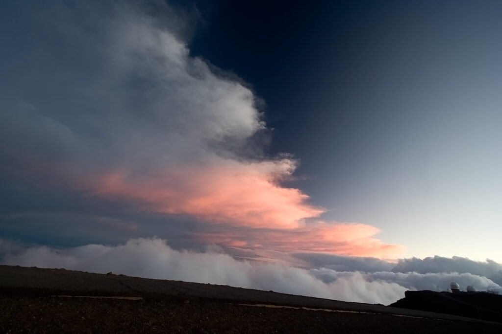 A breathtaking sky filled with dramatic clouds painted in hues of pink and orange, hovering above dark silhouetted hills.
