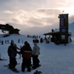 Christmas Skiers and snowboarders gathering near a ski lodge as the sun sets.