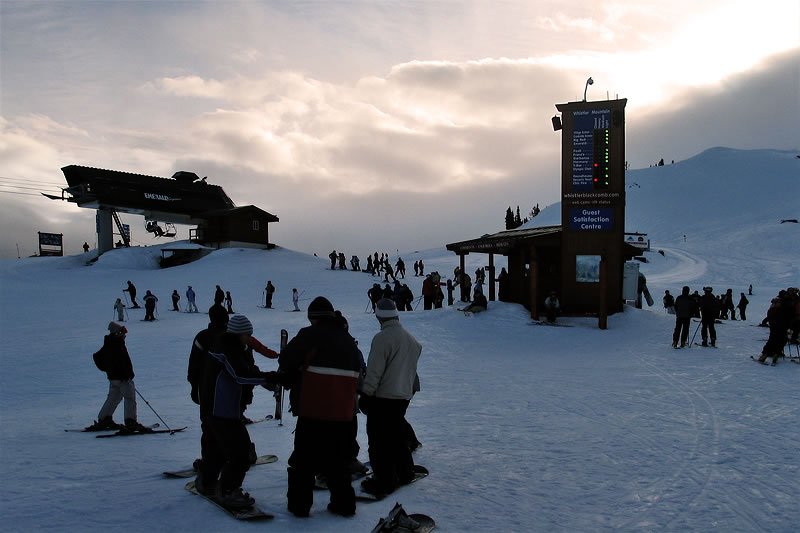 Skiers and snowboarders gathering near a ski lodge as the sun sets.