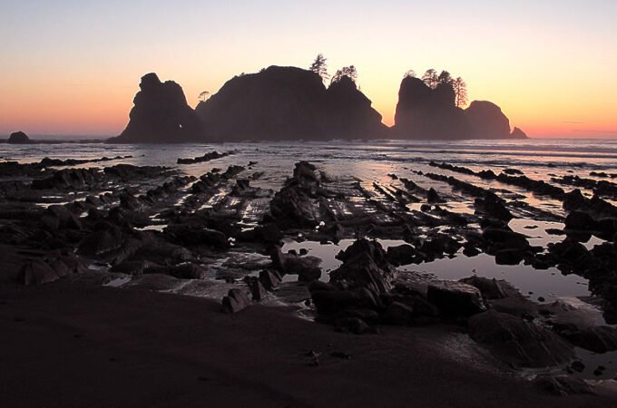A serene sunset over the iconic sea stacks at Cannon Beach, Oregon, casting a warm glow across the Pacific Ocean and rocky shoreline.