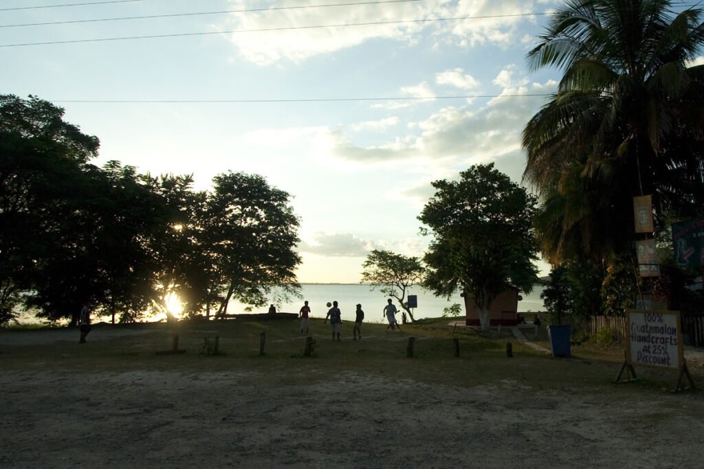 A group of people silhouetted against a sunset sky with palm trees and a tranquil beach in the background.