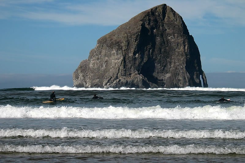 A surfer rides a wave near Haystack Rock in Cannon Beach, Oregon, showcasing the Pacific Northwest's coastal beauty.