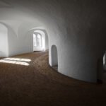 Mt. Constitution A surrealistic view of a curved interior space with arched windows and sunlight streaming in, creating patterns on the textured floor.