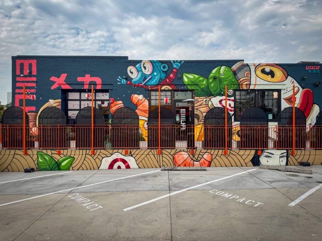 A colorful mural adorns the wall of a building labeled 'SUSHI FACTORY' with various sushi-themed artworks.
