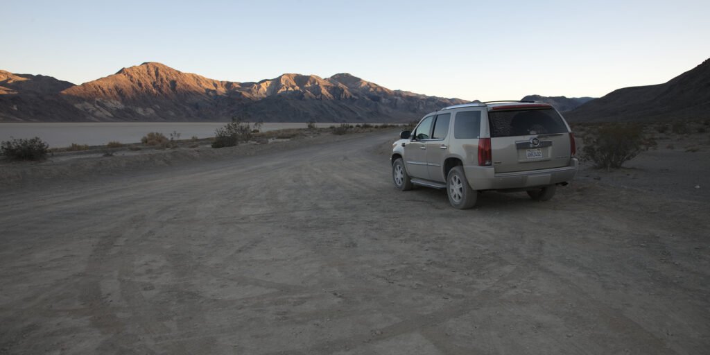 A silver SUV is parked on a dusty trail in a scenic mountainous landscape, capturing the essence of an adventurous outing.