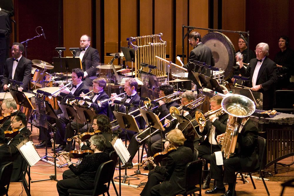 A symphony orchestra dressed in formal attire performs in a concert hall.