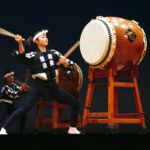 London Enthusiastic performers playing large taiko drums on stage under bright lights