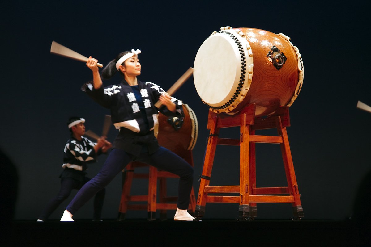 KODO Enthusiastic performers playing large taiko drums on stage under bright lights