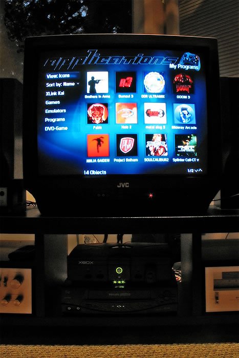 A television screen illuminated with a media user interface menu. The TV is placed on a stand above various electronic devices in our home.