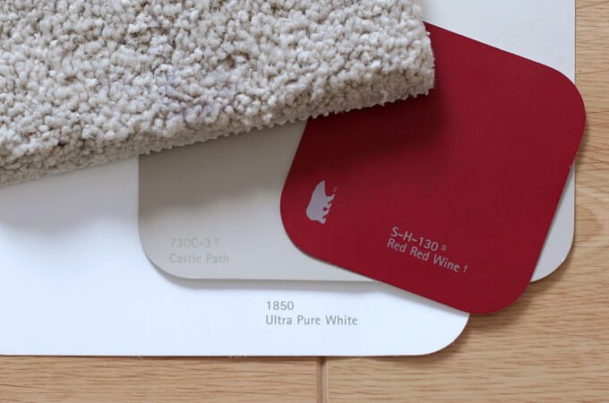 A close-up view of a textured white carpet alongside red wine and ultra pure white color swatches on a wooden surface.