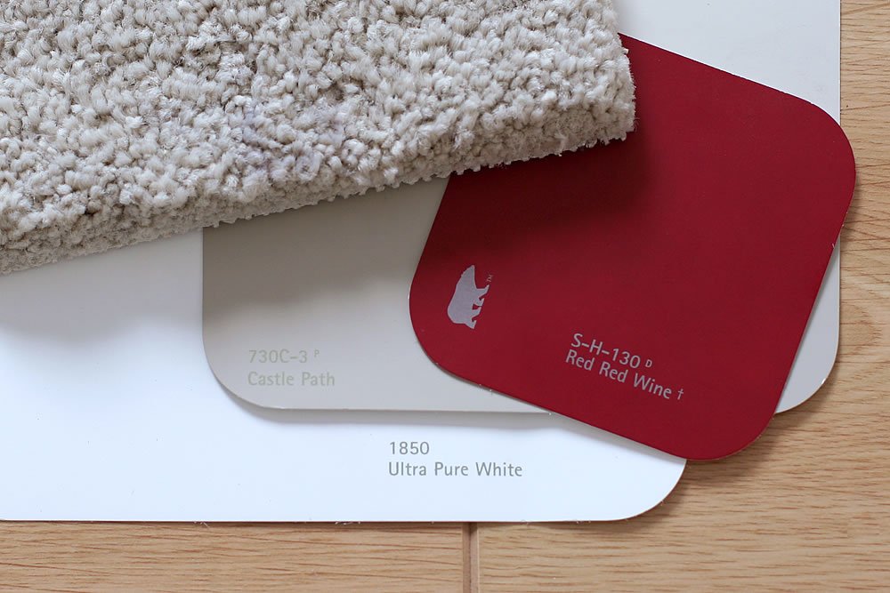 A close-up view of a textured white carpet alongside red wine and ultra pure white color swatches on a wooden surface.