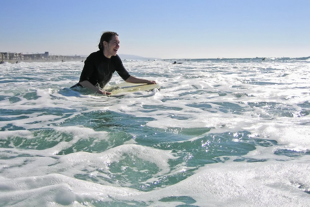 A surfer paddles on a vibrant ocean wave. She smiles as she feels the thrill of the ride.