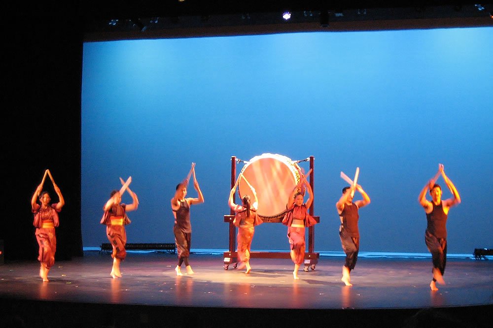 Dancers performing a traditional hula dance with a large drum on stage.