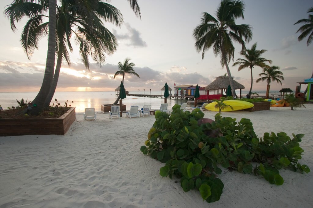 A serene tropical beach scene featuring palm trees and colorful cabanas under a partly cloudy sky.