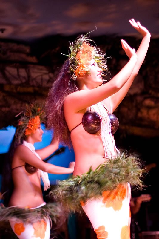 A woman performing a hula dance with traditional attire and greenery accents.