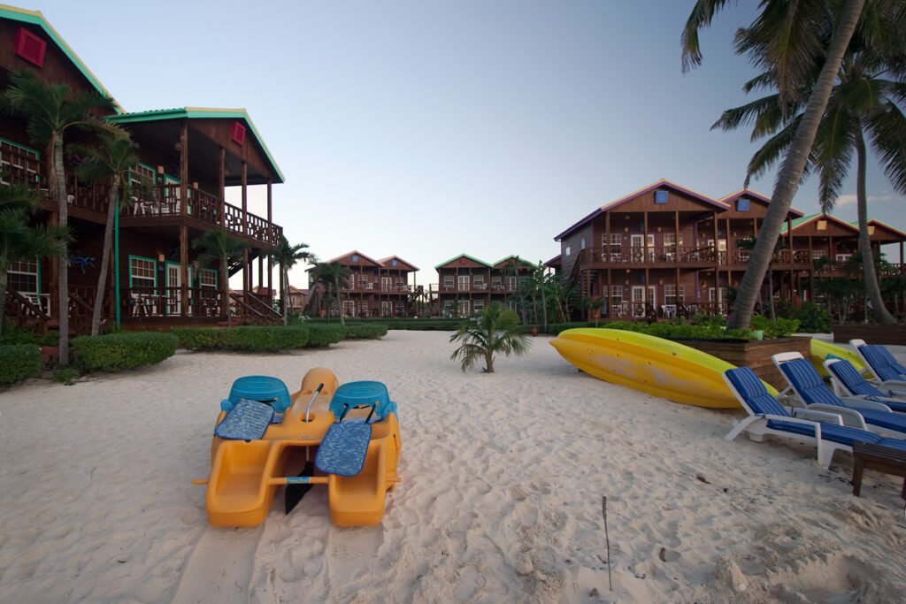A serene beach resort featuring vibrant beach chairs, palm trees, and warm wooden bungalows under a clear sky.