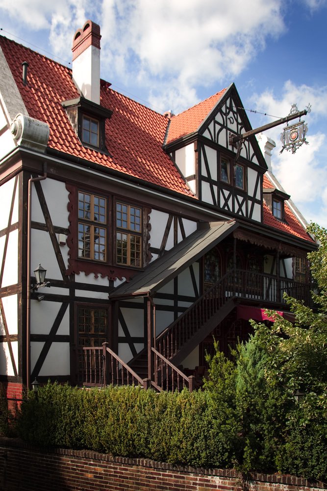 A classic Tudor-style house featuring a distinctive red-tiled roof and timber framing under a blue sky.