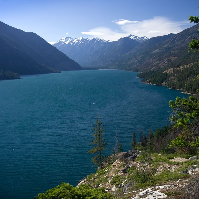 Stunning turquoise lake surrounded by mountains with snow-capped peaks under a clear blue sky.