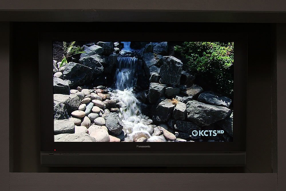 A television displays a rocky landscape with a cascading waterfall, surrounded by greenery.